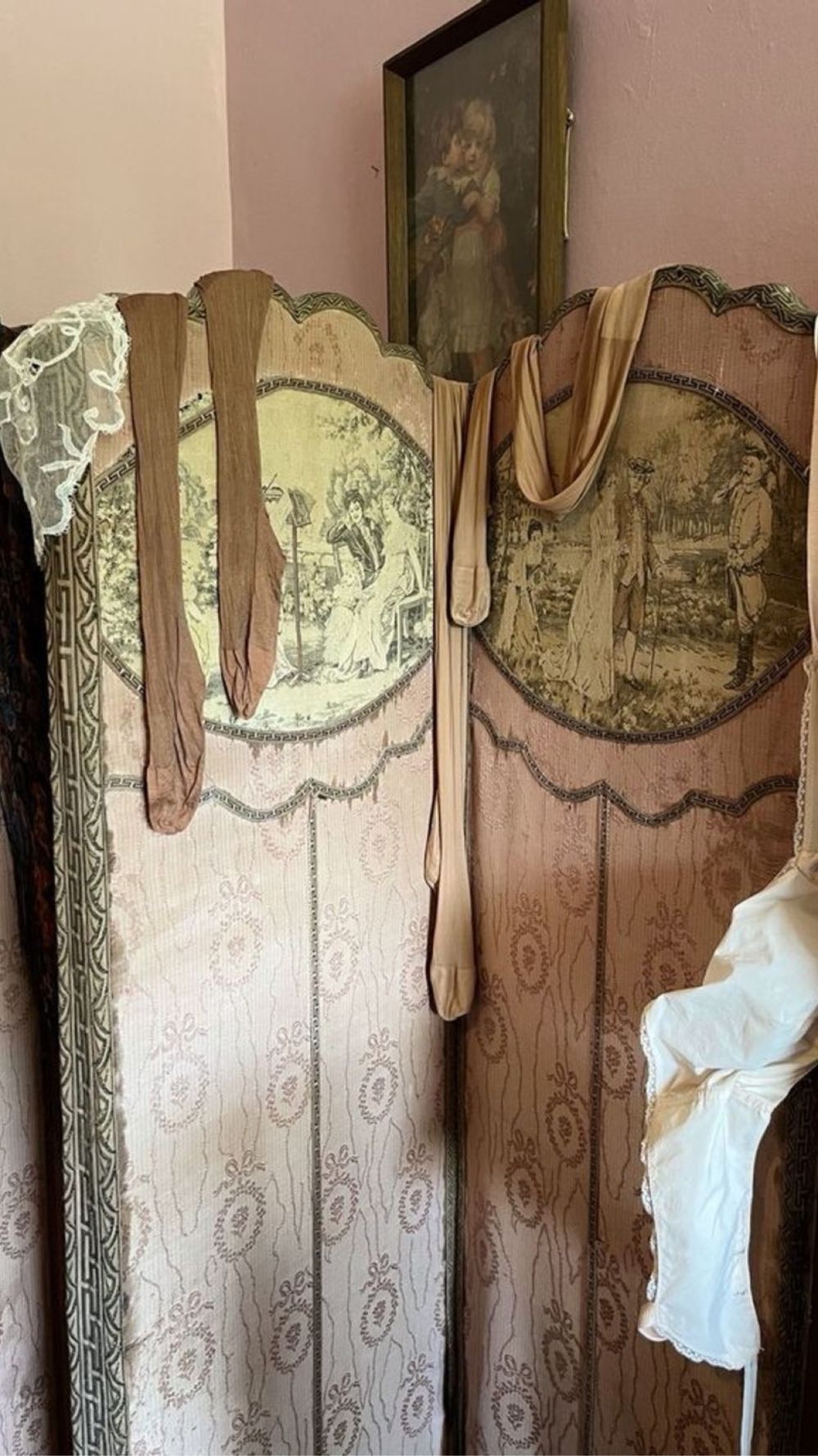 An antique tapestry dressing screen with silk stockings draped over the top